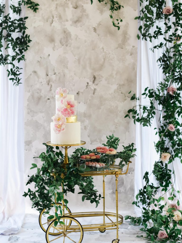 wedding cake displayed on a vintage gold bar cart in front of watercolor backdrop