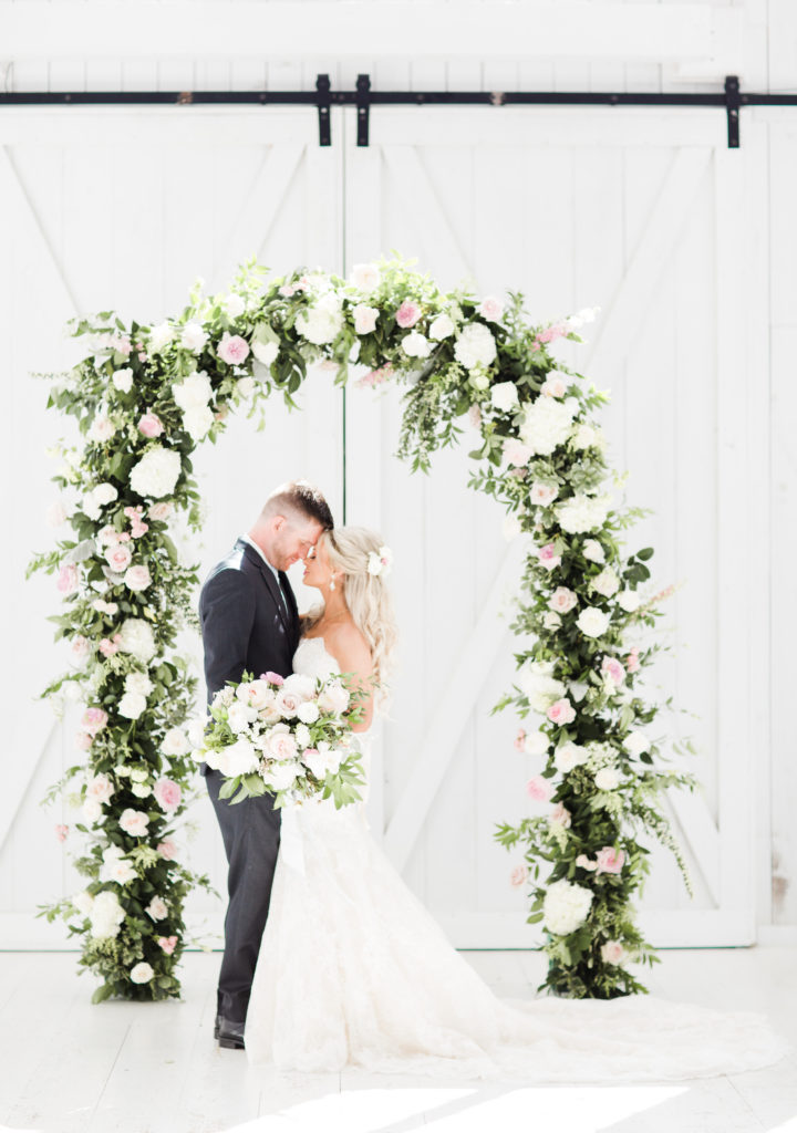 the bride and groom standing under their aisle floral arch at the White Sparrow Barn