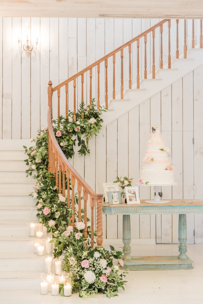 Wedding cake displayed by a staircase covered in florals