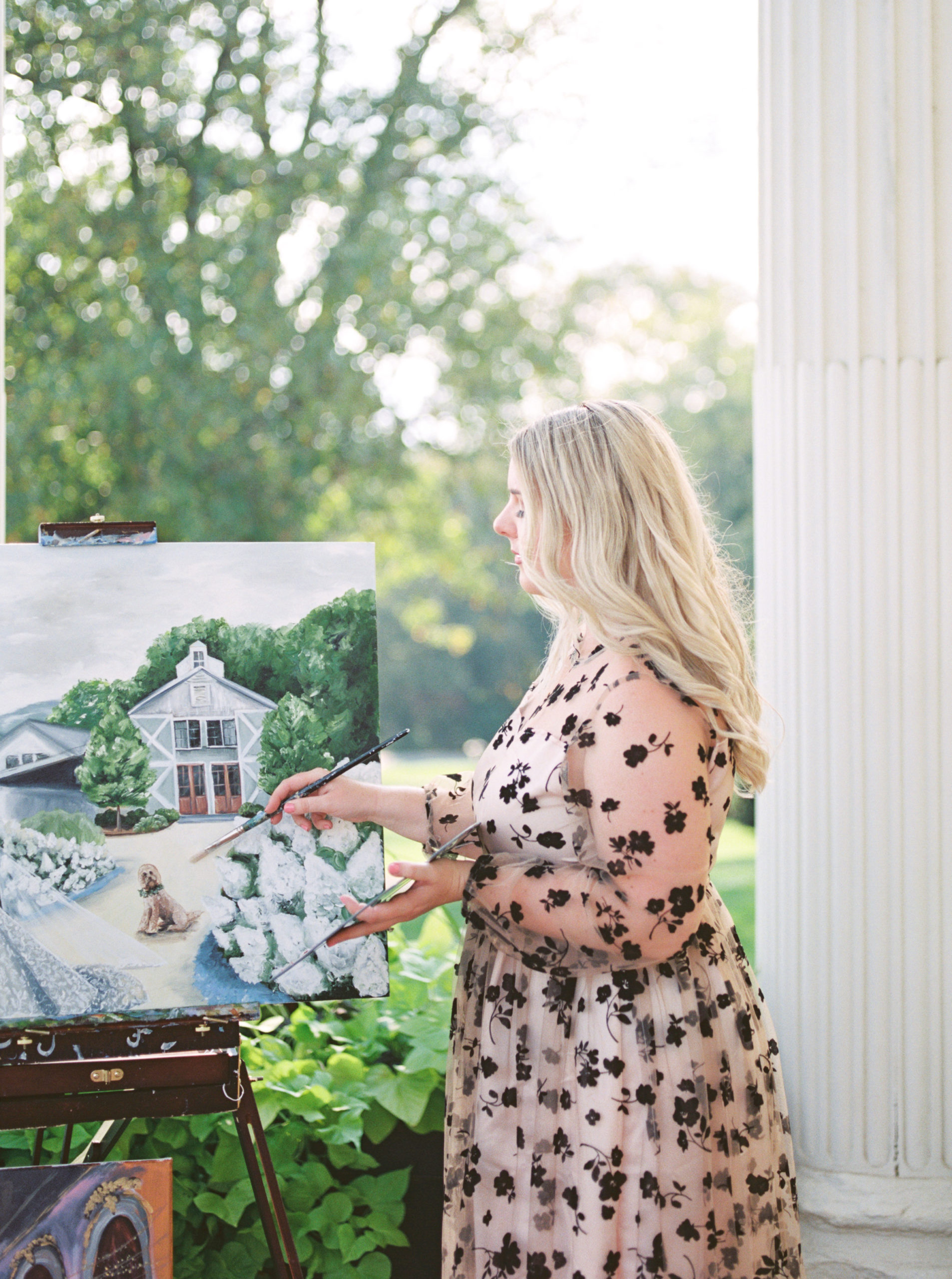 Live wedding painter By Brittany Branson works on a painting in Leesburg, Virginia. She wears a pink dress with black lace overlay.