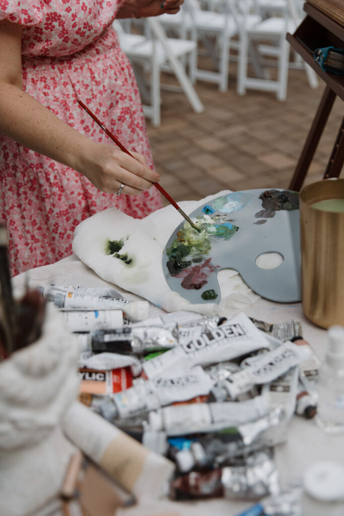Live wedding painter, Brittany Branson, is dipping her brush into a palette of paint.
