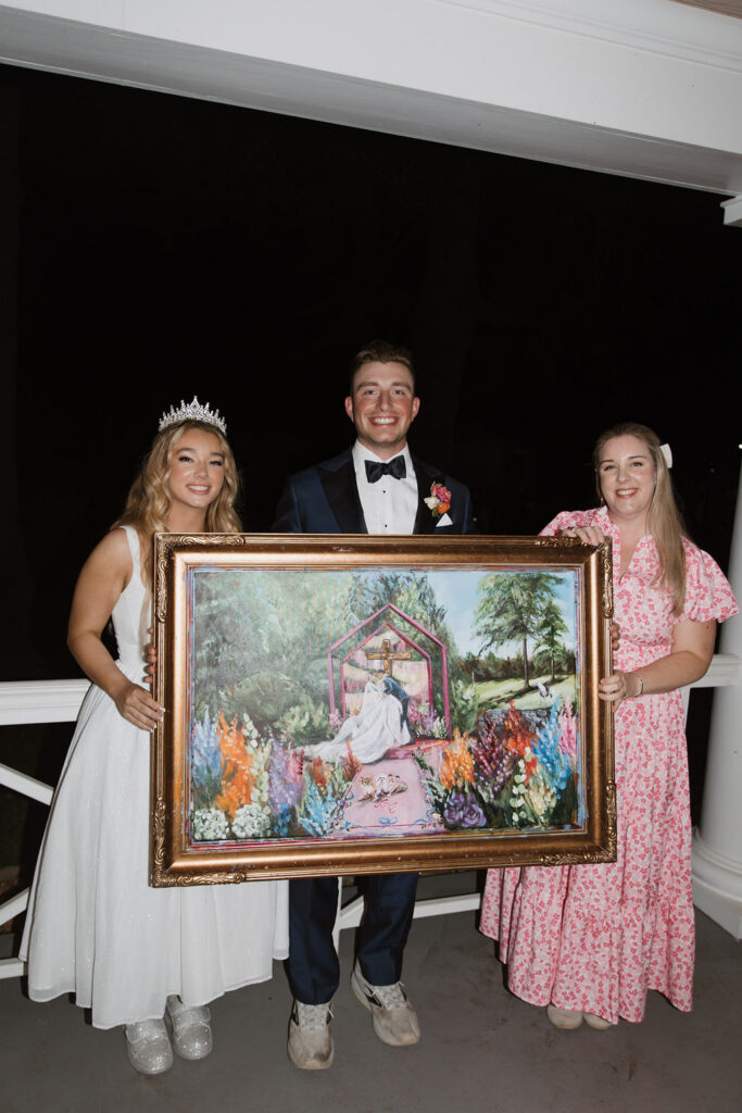 Baylen, Colin, and Brittany stand together as the three of them hold up the completed live painting of this wedding.